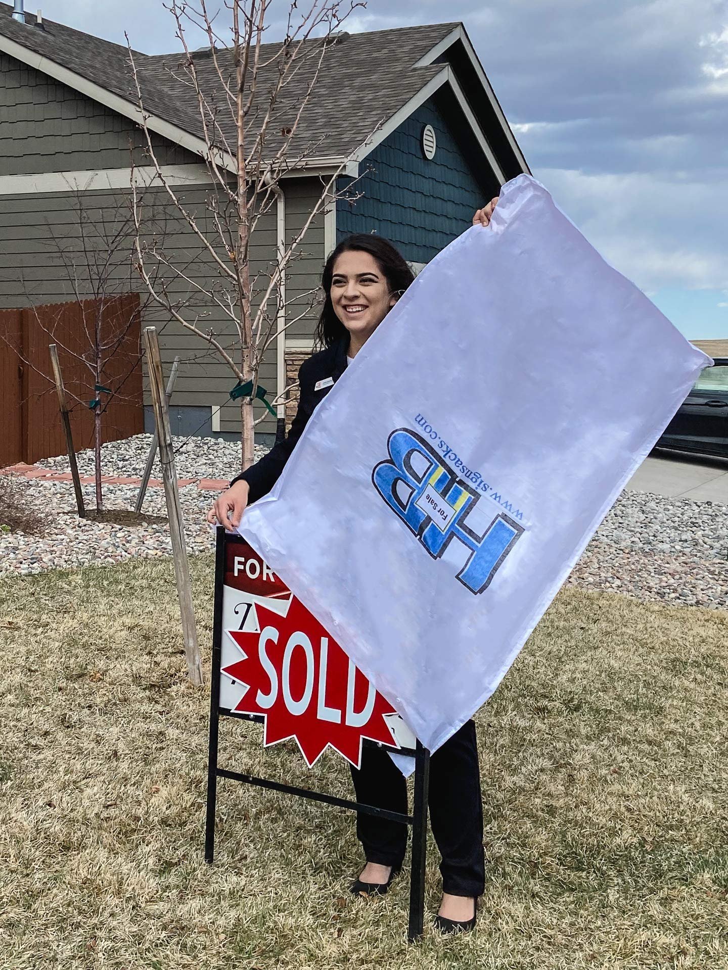 Real estate agent holding a "Sold" sign cover in front of a house